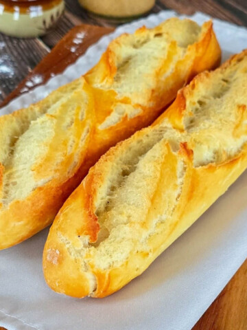 Deux baguettes de pain maison dorées et croustillantes posées sur un linge blanc et une planche en bois.