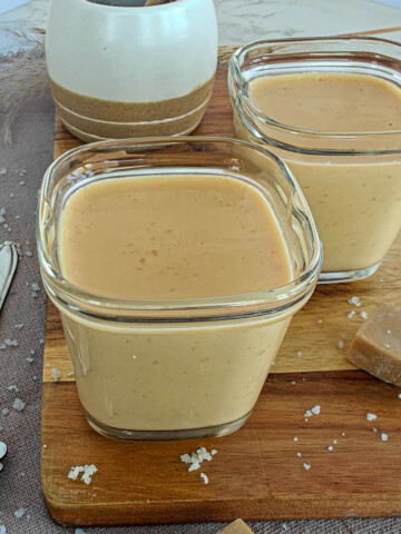 Deux crèmes dessert au caramel avec une pointe de sel; sur une planche de bois, avec des fudges au caramel.