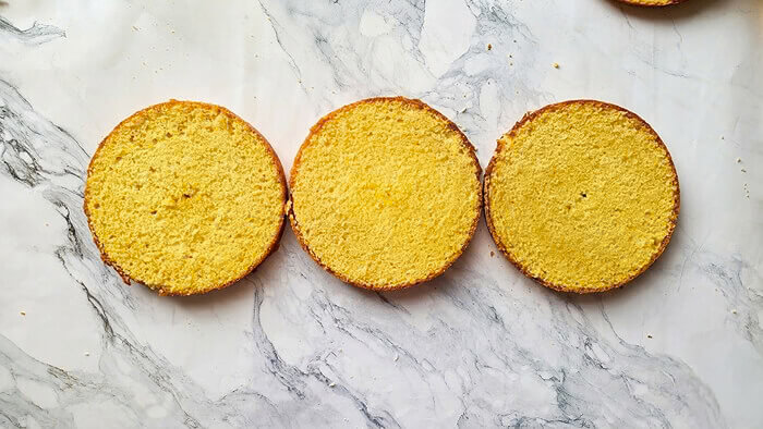 molly-cake-tranches-horizontales-vue-dessus Trois tranches horizontales et régulières de génoise Molly Cake, alignées sur un plan de travail en marbre, prêtes pour le montage.