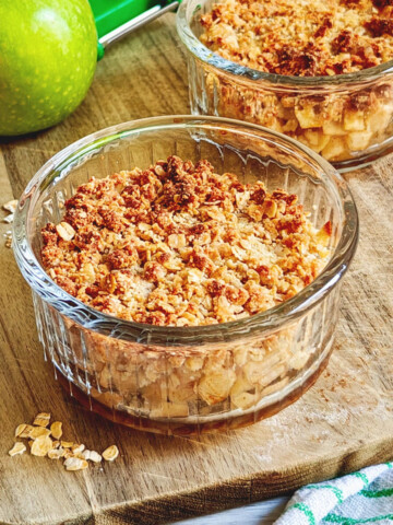 Deux ramequins transparents remplis de crumble pomme healthy sur une planche de bois, pomme verte en arrière.