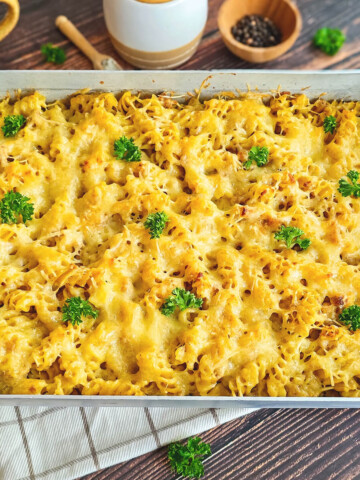 Vue d'ensemble d'un plat à gratin rectangulaire contenant des pâtes au thon avec une croûte de fromage fondu bien dorée, décoré de bouquets de persil frais, posé sur un torchon à carreaux.