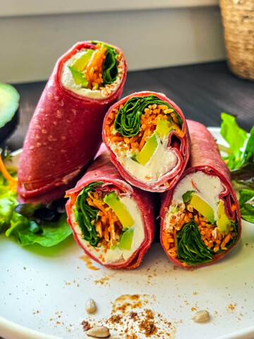 Un wrap avocat, chèvre et carotte sur une assiette blanche, laitue et avocat sur le côté.