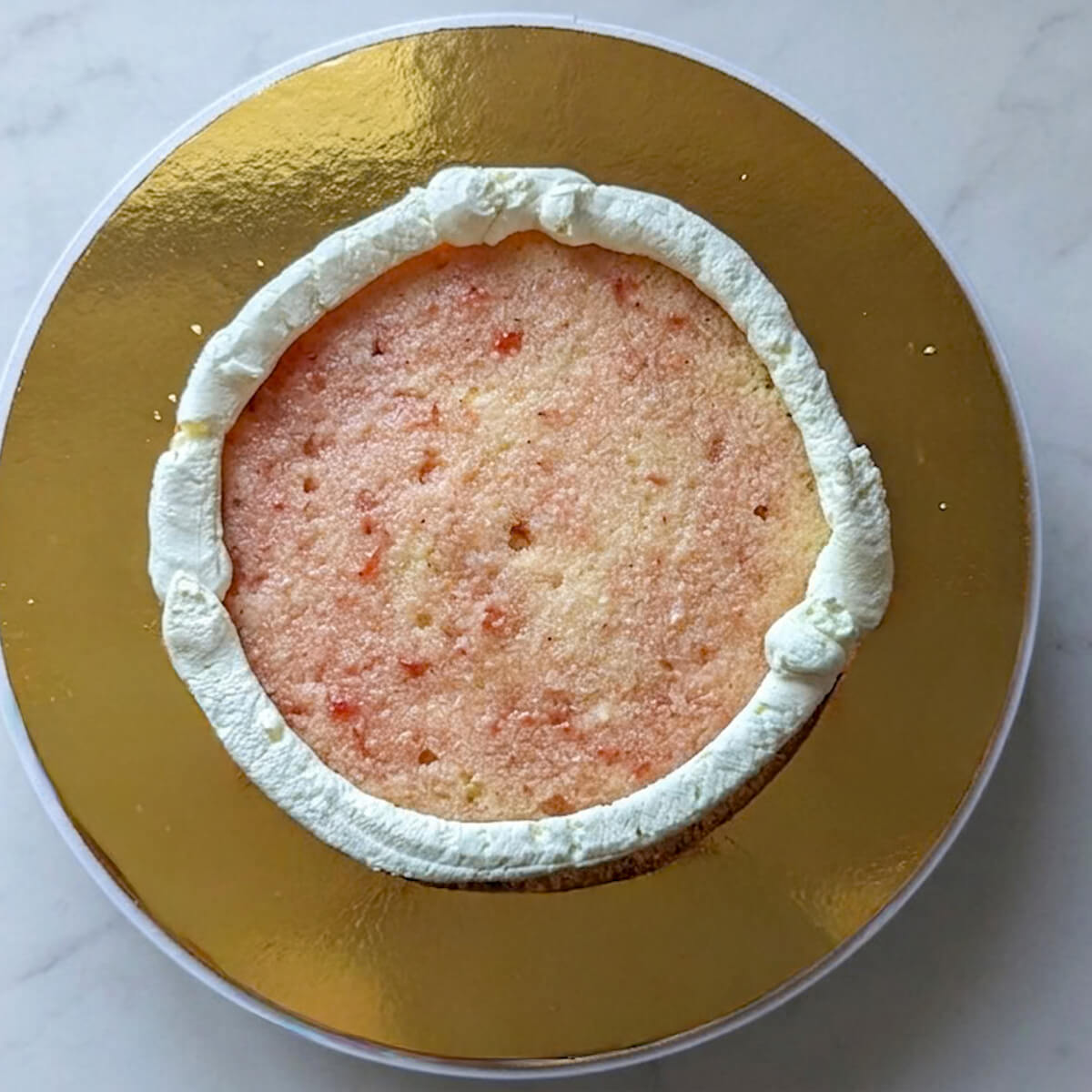 2-boudin-de-chantilly-mascarpone-layer-cake-fraise Photographie en plongée montrant un boudin de chantilly mascarpone pochée sur le pourtour extérieur d'un disque de biscuit imbibé au sirop de fraises.
