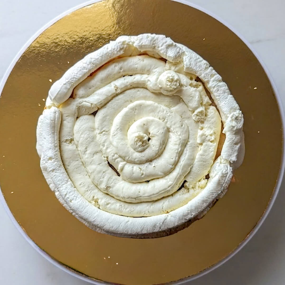 3-ganache-montér-vanille-layer-cake-fraise Gros plan en vue de dessus montrant le pochage en spirale d'une onctueuse ganache montée à la vanille à l'intérieur du boudin de protection sur la base du layer cake.