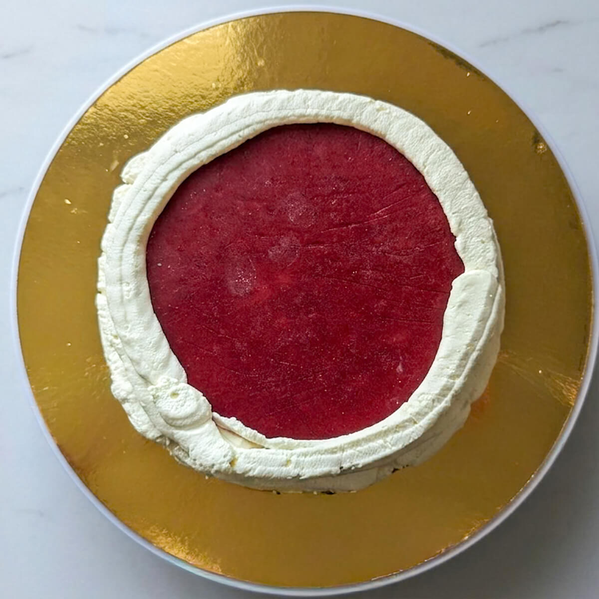 4-insert-gelée-layer-cake-fraise Vue aérienne d'un disque d'insert gélifié aux fraises fraîches rouge vif, parfaitement inséré au centre du boudin de crème sur une couche de Molly cake.