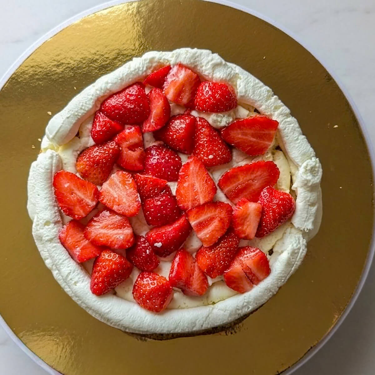 5-2e-etage-fraises-coupées-layer-cake-fraise Photographie rapprochée en vue de dessus montrant une généreuse couche de morceaux de fraises fraîches et juteuses disposés à l'intérieur du barrage de crème d'un layer cake en cours de montage.