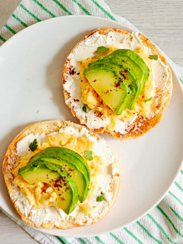 Un bagel toasté garni de fromage frais, d’œufs brouillés onctueux et de tranches d'avocat frais, saupoudré d'épices et de coriandre.