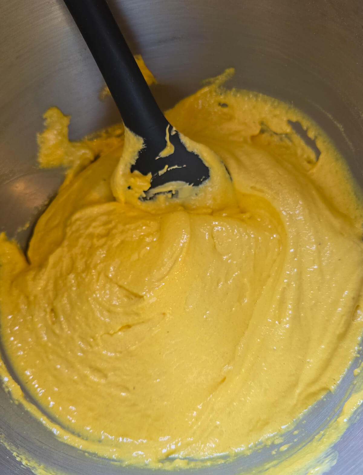 macaronnage-macarons-citron Étape du macaronnage dans un cul-de-poule en inox : mélange de la meringue jaune et de la poudre d'amande avec une maryse noire pour obtenir un ruban lisse.