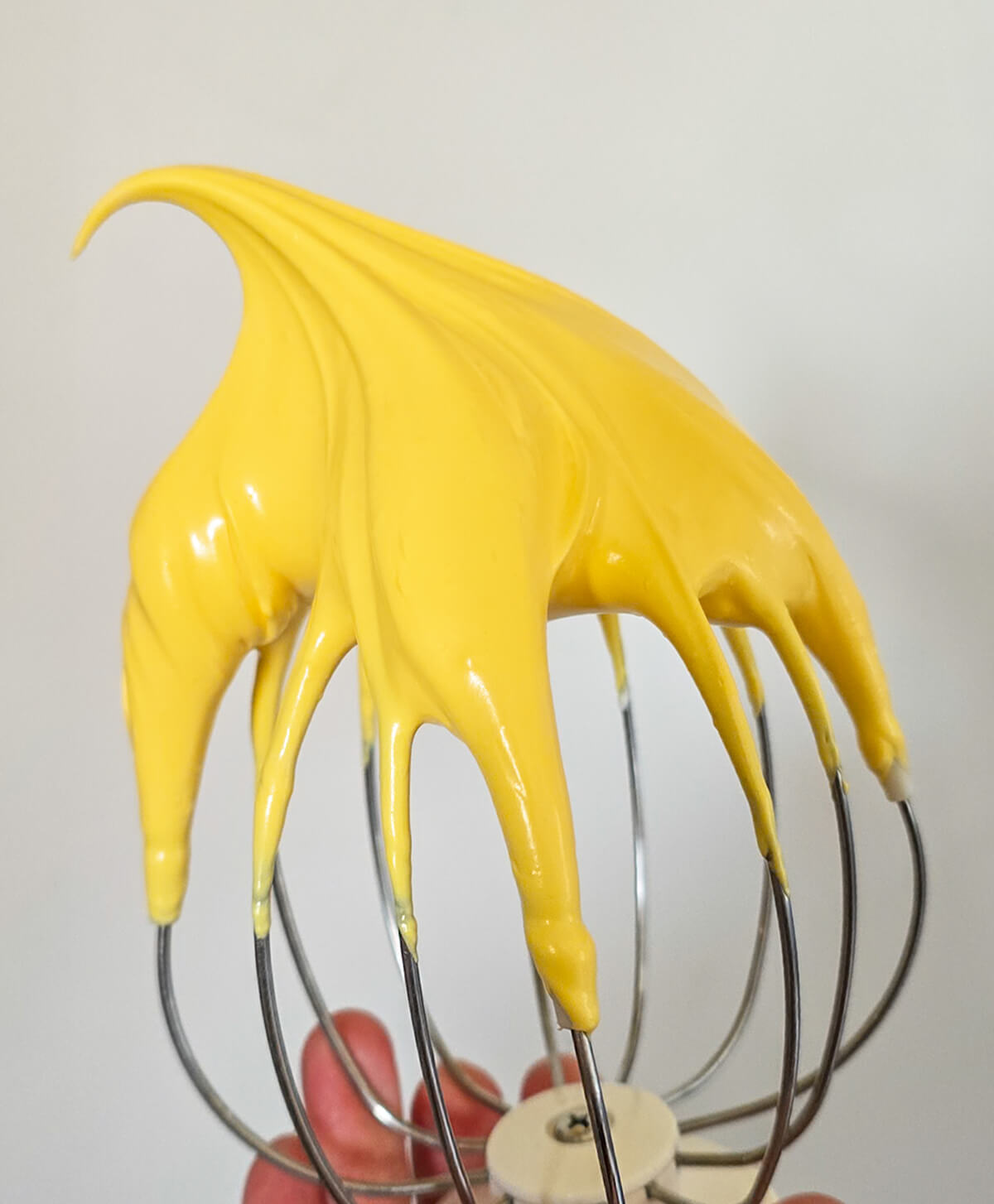 meringue-italienne-macarons-citron Meringue italienne d'un jaune éclatant sur un fouet de pâtissier, avec un bec d'oiseau bien ferme pour la préparation de coques de macarons au citron.