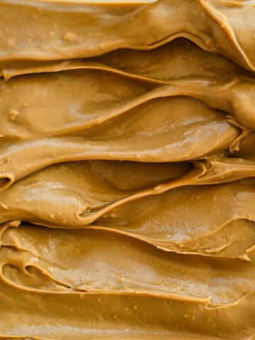 La surface d'une ganache au café dans un plat. La texture est riche, lisse et brillante, avec des ondulations profondes et des marques de spatule qui créent des motifs ondulés.