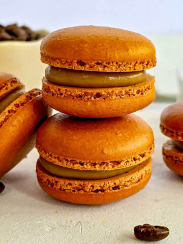 plusieurs macarons au café, de couleur brune, fourrés d'une ganache crémeuse, disposés sur un fond blanc.