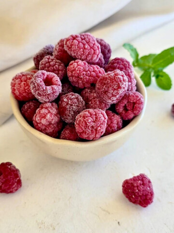 Des framboises surgelées dans un petit bol blanc, menthe fraîche et framboises sur le côté.