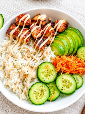 Un poké bowl composé de morceaux de saumon cuits, rondelles de concombre, tranches d'avocat et de carottes râpées, le tout nappé d'une sauce mayonnaise sriracha.