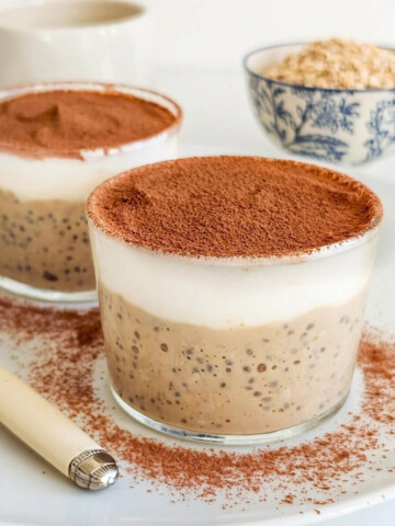 Gros plan de deux verrines de pudding d'avoine et chia au café, surmontées d'une couche de yaourt blanc et de cacao amer.