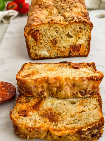 Un cake au chorizo coupé en tranches, sur une planche marbrée blanche, rondelles de chorizo et tomates cerises sur les côtés.