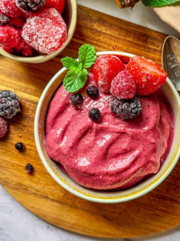 Un bol rempli de glace fruits rouges, avec des fruits surgelés sur le dessus, sur une planche de bois.