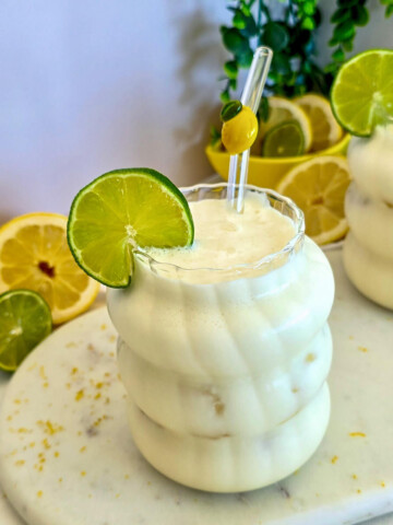 Gros plan d'une limonade brésilienne au citron vert dans un verre givré ondulé, surmonté d'une tranche de citron vert et d'une paille avec un motif de citron jaune.