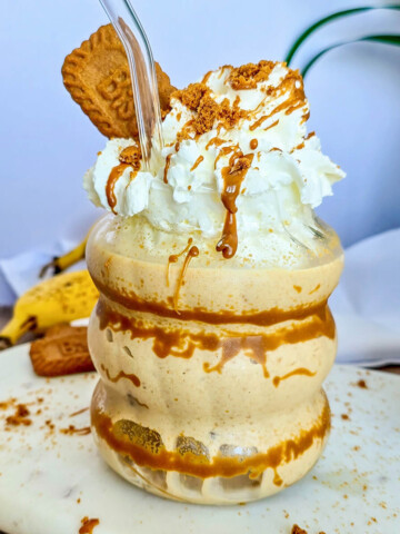 Milkshake banane et spéculoos dans un verre ondulé, nappé de coulant de spéculoos, surmonté de crème chantilly, d'un biscuit Biscoff et d'une paille en verre.