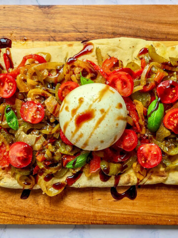 Vue de dessus d'une pinsa généreusement garnie de poivrons colorés, de tomates cerises fraîches, de basilic et d'une burrata centrale avec un filet de balsamique.