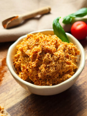 Des rillettes de poulet dans un bol blanc, sur une planche de bois, tomates cerises en arrière plan.